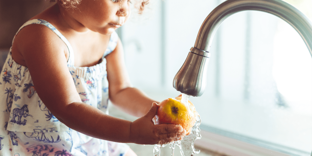 A child washing an apple in a kitchen sink at The Fredd Townhomes in San Antonio, Texas