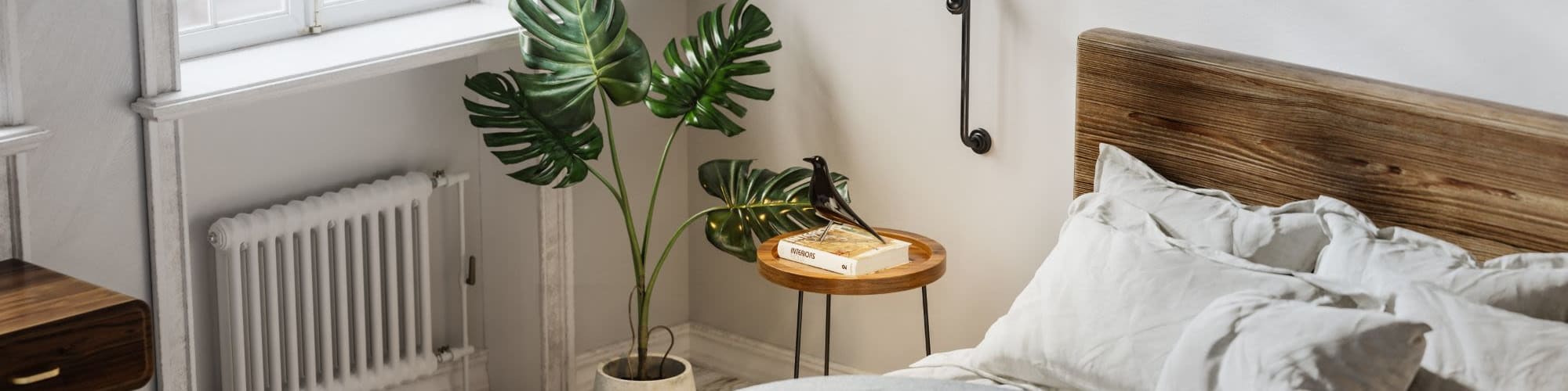 Bedroom with Cozy Bed, a Night Stand, and Green Potted Plant Next to a Window at 1221 Vallejo Apartments in Novato, California