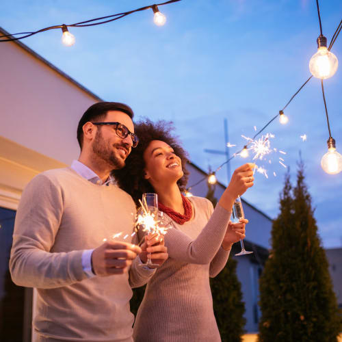Resident couple out on their private balcony holding sparklers at dusk at Hyde Park at Montfort in Dallas, Texas