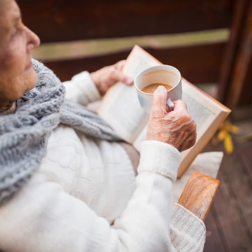 Resident reading a book with some coffee at Riverside Oxford Memory Care in Ft. Worth, Texas
