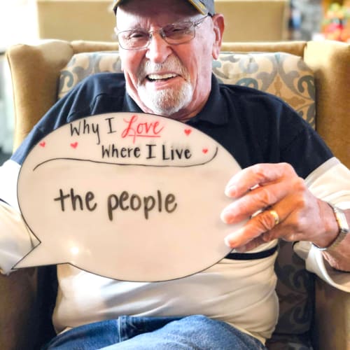 A resident holding a sign that says 'Why I love where I live: The people!' at a Oxford Senior Living community