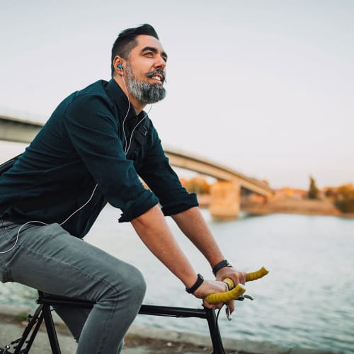 Well-groomed man listens to Nathanial Rateliff with in-ear headphones while riding a fixed-gear bicycle along the banks of the South Platte River near Hawthorne Hill Apartments in Thornton, Colorado