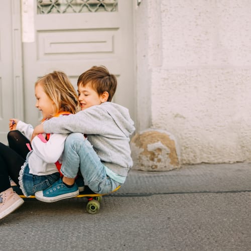 Two kids riding down the hill on a skateboard at Aspen Pines Apartment Homes in Wilder, Kentucky