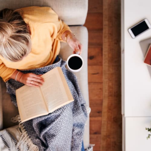 Resident laying on the couch with her favorite book and a cup of coffee at 700 Constitution in Washington, District of Columbia