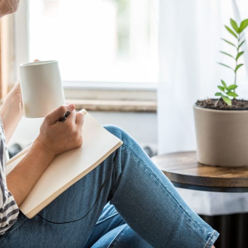 Resident writing while she drinks a cup of coffee on the couch at Dorchester House in Washington, District of Columbia