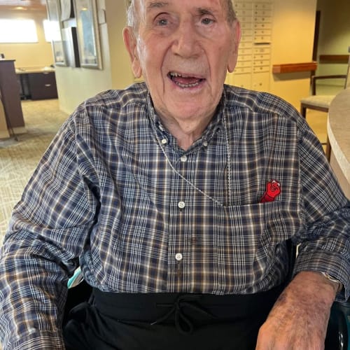 Masked caretaker talking to a seated resident at The Oxford Grand Assisted Living & Memory Care in Wichita, Kansas