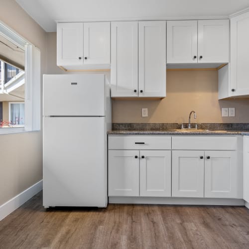 Open kitchen with white cabinetry and wood-style plank flooring at Royal Gardens Apartments in Livermore, California