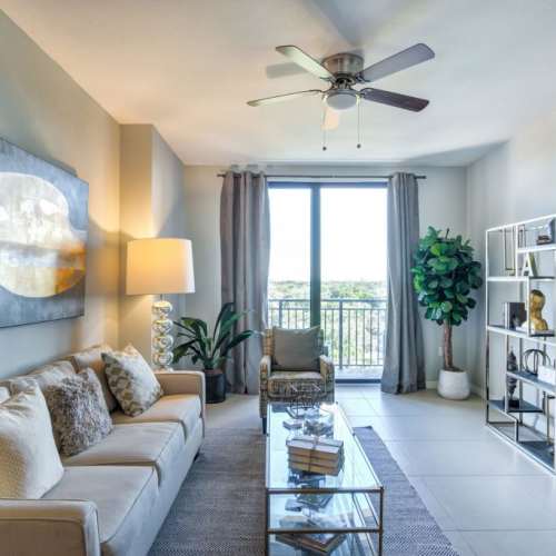 Spacious living room with couch, coffee table, and access to balcony through a sliding glass door at Club Prado in West Miami, Florida