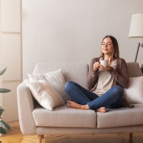 Woman drinking coffee on her couch at Narrows Pointe Apartments in Tacoma, Washington