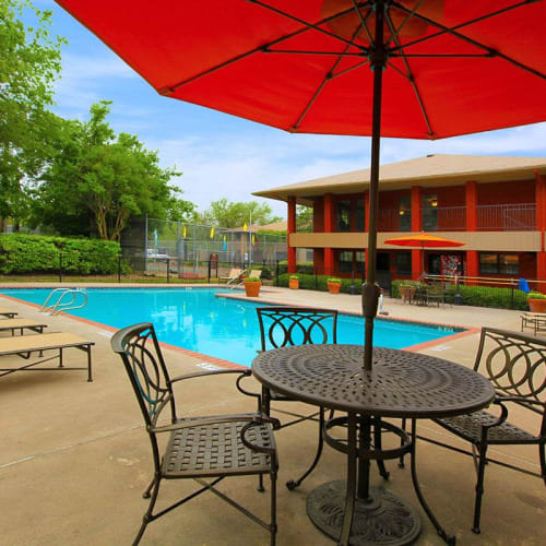 An outdoor table with an umbrella beside the swimming pool at The Granite at Tuscany Hills in San Antonio, Texas