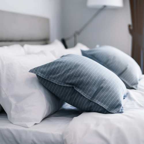 A freshly made bed with crisp white sheets and blue throw pillows at Ascent Apartment Homes in Asheville, North Carolina