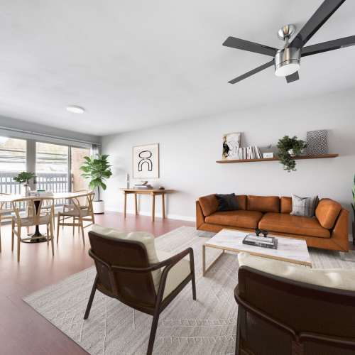 Spacious living room with a comfortable couch, ceiling fan and large window at Lantera Apartments in Seattle, Washington