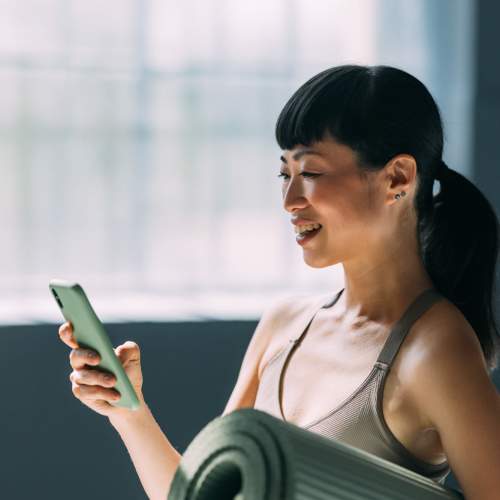 A woman holding a yoga mat and looking at her phone in the fitness center at The Lowe in Savannah, Georgia