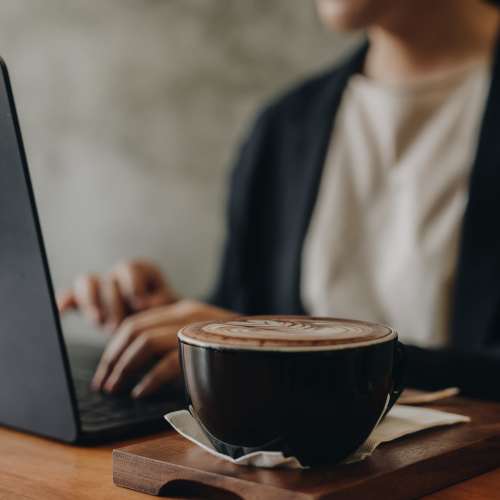 Woman working remotely on her laptop with a latte at UCA Apartment Homes in Fullerton, California