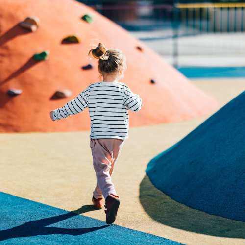 Child running joyfully in a colorful playground with climbing structures at Alice Patricia Apartments in Waukee, Iowa