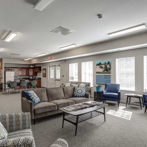 Bright community lounge with comfortable seating, large windows, and a kitchenette in the background at Brookside Commons in Traverse City, Michigan