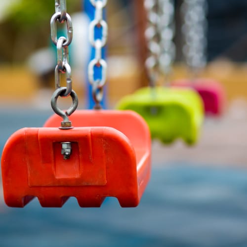 Colorful swings hanging from chains in a playground area with soft ground surface at Winston Commons in Pontiac, Michigan