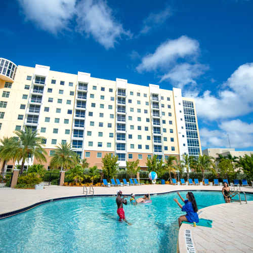 Resort-style pool surrounded by palm trees and lounge chairs with families enjoying the water at Bayview Student Living in North Miami, Florida