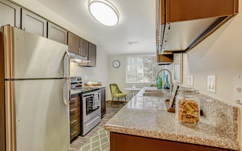Fully equipped kitchen with brown cabinets, stainless steel appliances and a view of the dining room at Walnut Grove Landing Apartments in Vancouver, Washington