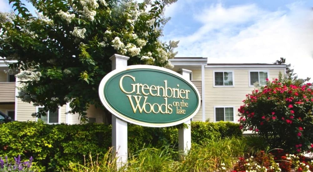 Exterior signage on sunny day with flowers at Greenbrier Woods Apartments in Chesapeake, Virginia
