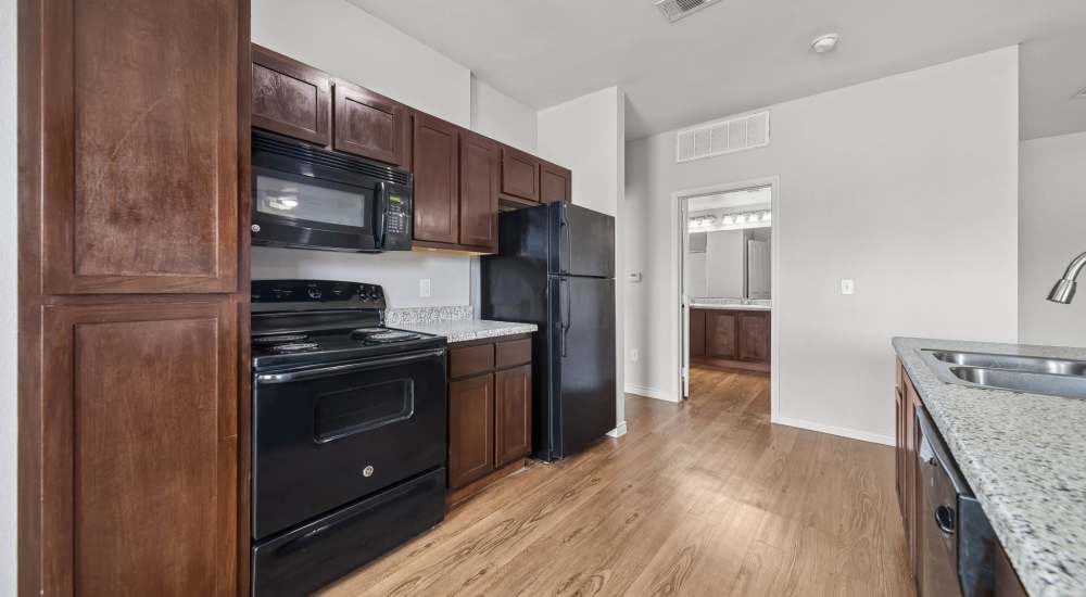Apartment kitchen with wood cabinets and black appliances at Sunset Lodge in Odessa, Texas
