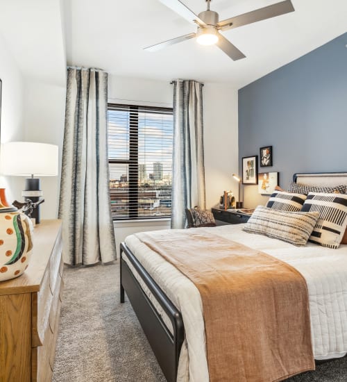 Bedroom with large window, ceiling fan, accent wall, and carpet The Margaret at Riverfront in Dallas, Texas