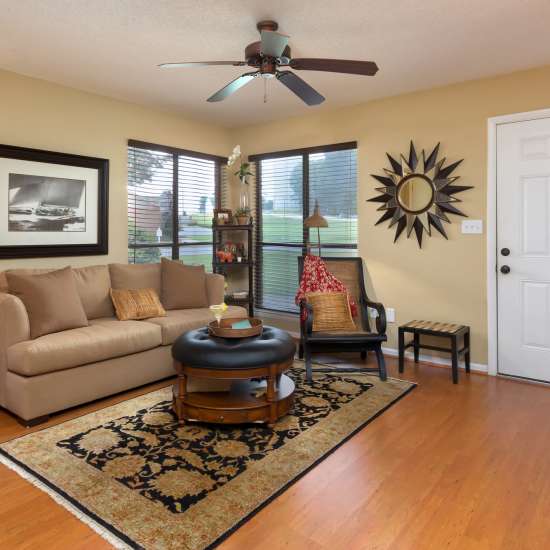 Spacious living room with hardwood flooring, ceiling fan, comfortable couch and large windows at The Arbors On Taylor in Montgomery, Alabama