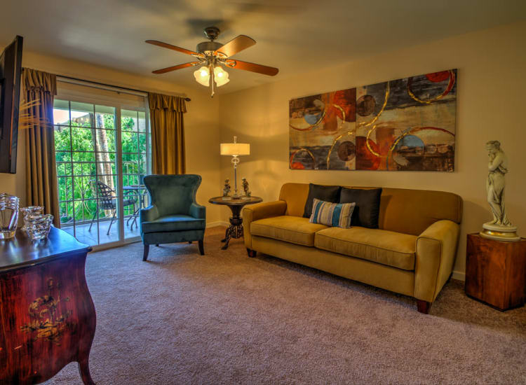 Plush carpeting and a ceiling fan in the open-concept living space of a model senior apartment at Bella Vista Senior Living in Mesa, Arizona