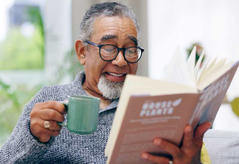 Resident drinking coffee and reading a book at Pines of Newmarket in Newmarket, New Hampshire