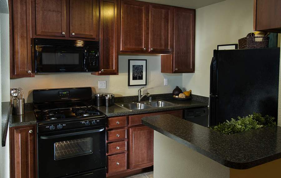 Apartment kitchen with wooden cabinets and black appliances at UCA Apartment Homes in Fullerton,California