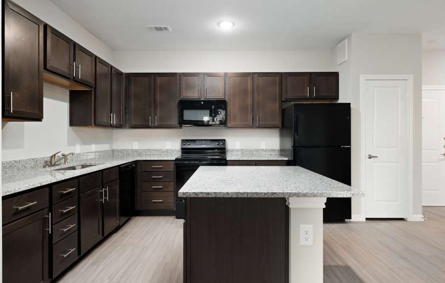 Modern kitchen with granite countertops, stainless steel appliances, dark cabinetry, and wood-style flooring at Preserve at Gresham Lake in Raleigh, North Carolina