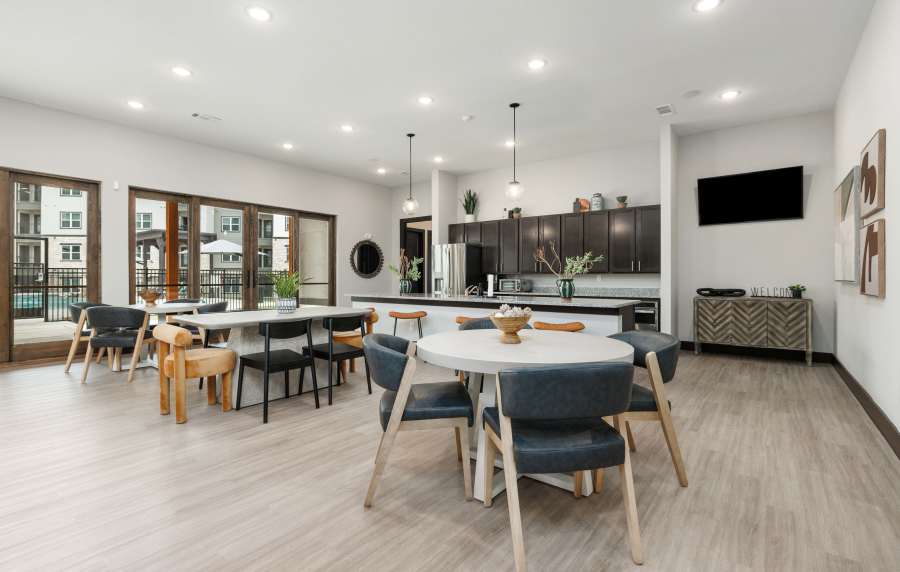 Bright community lounge with wood-style flooring, modern kitchen, and large windows overlooking the pool area at Preserve at Gresham Lake in Raleigh, North Carolina