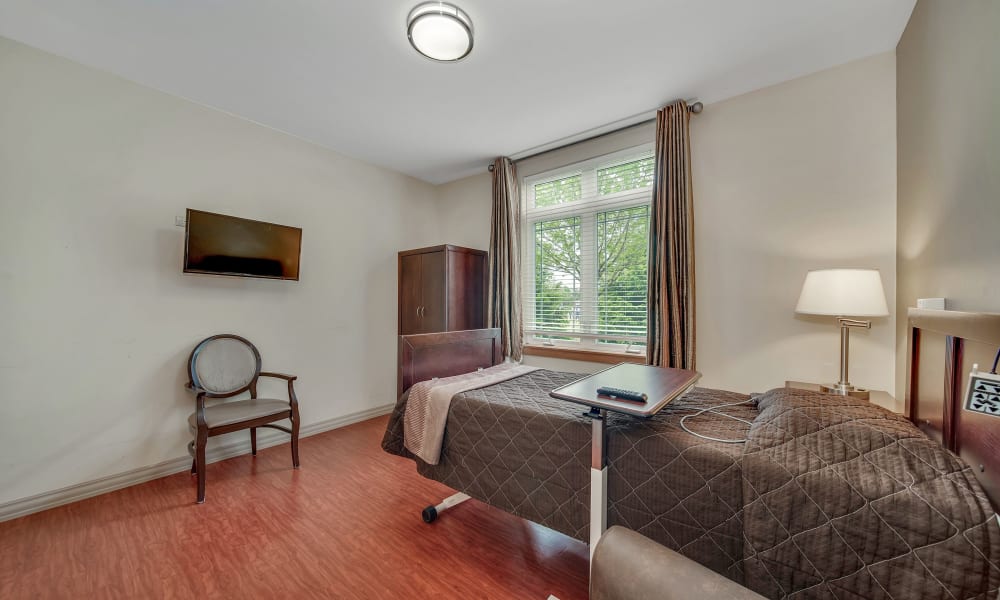 Single-resident transitional care room with a tv, hardwood floors, and a large window at Fair Oaks Health Care Center in Crystal Lake, Illinois