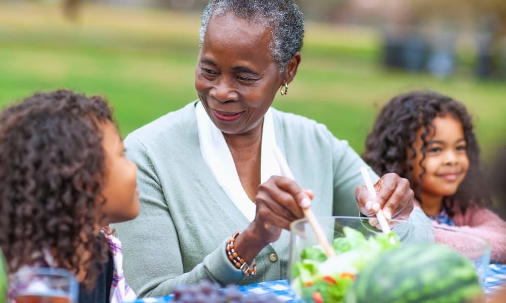 Resident serving fresh salad to her grandchildren at a picnic at a Cascade Senior Living Services community