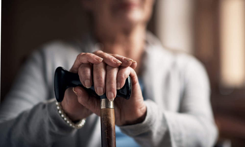 Resident resting her hands on a cane while sitting near a window at a Cascade Senior Living Services community
