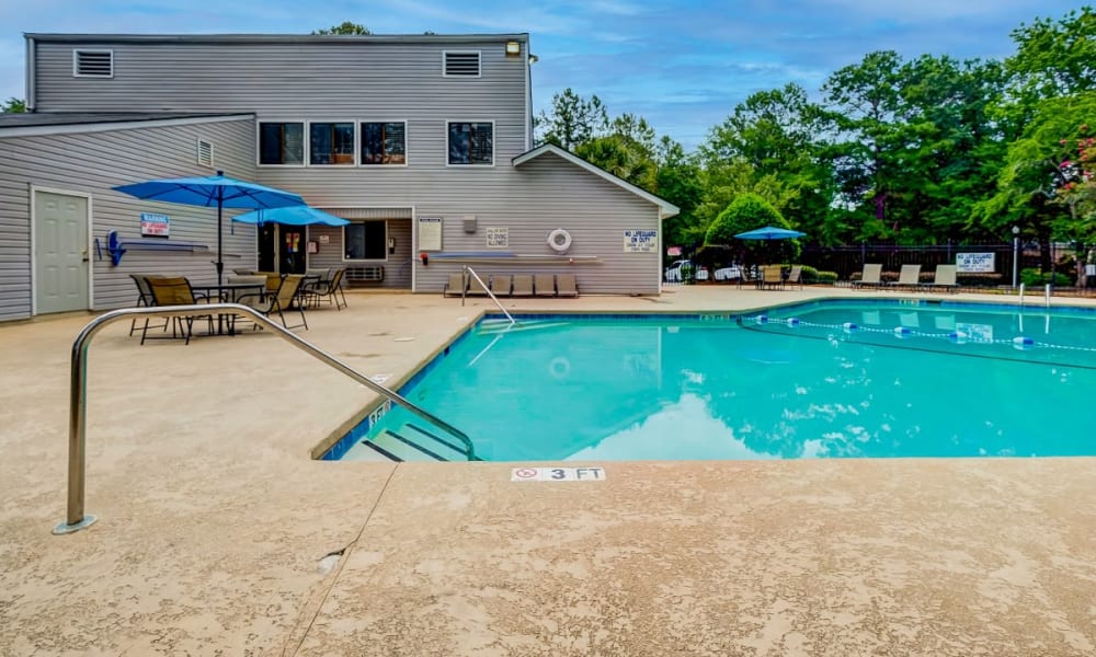 swimming pool with tables, chairs and umbrellas on pool deck at Forestbrook Apartments & Townhomes in West Columbia, South Carolina