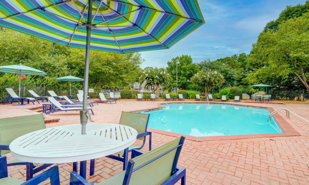 Tables, chairs, and umbrellas around swimming pool at Grove at Stonebrook Apartments & Townhomes in Norcross, Georgia
