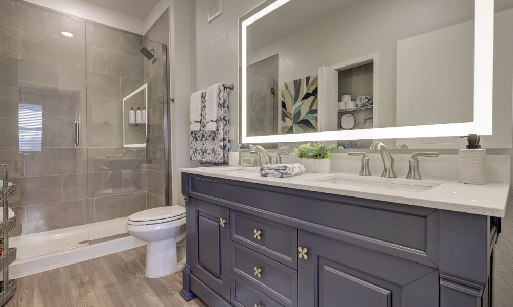 Luxurious model bathroom with wood cabinetry and large vanity mirror in a home at The Vivien in Vero Beach, Florida