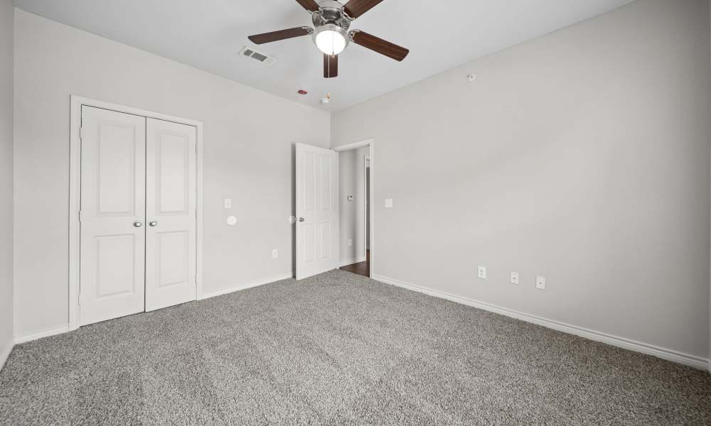 Carpeted bedroom with lighted ceiling fan and entry door and closet door in background at Sunset Lodge in Odessa, Texas