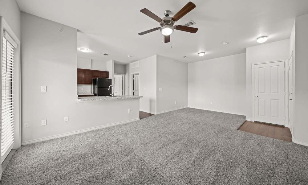 Unfurnished, carpeted living room with kitchen and entry door in background at Sunset Lodge in Odessa, Texas