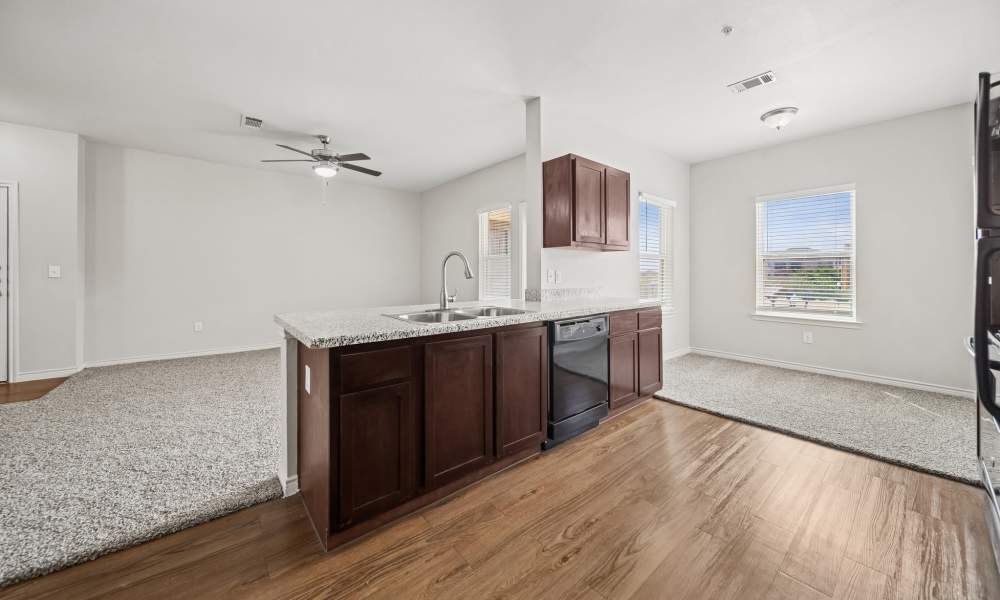 Kitchen with wooden cabinets and black appliances with living room in the background on the left, and the dining room in the background on the right at Sunset Lodge in Odessa, Texas