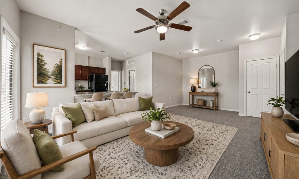 Furnished, carpeted living room with kitchen and entry door in background at Sunset Lodge in Odessa, Texas