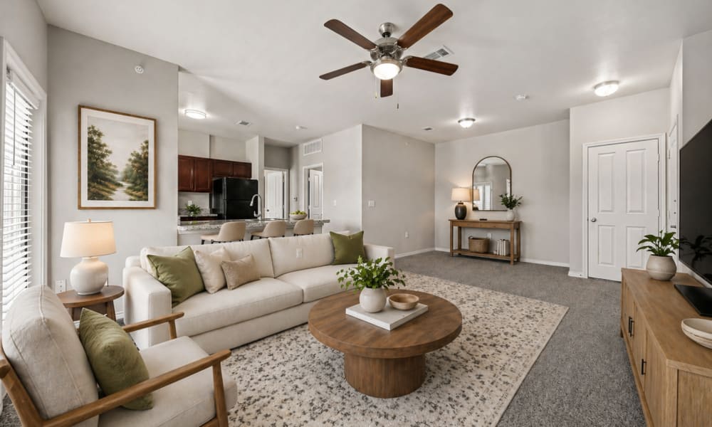 Furnished, carpeted living room with kitchen and entry door in background at Sunset Lodge in Odessa, Texas
