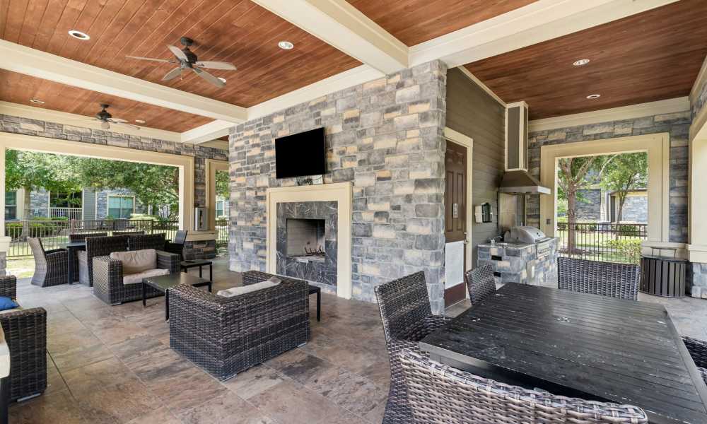 Covered outdoor patio with dining tables, sofas, and coffee tables, and a mounted TV at Plantation Park Apartments in Lake Jackson, Texas
