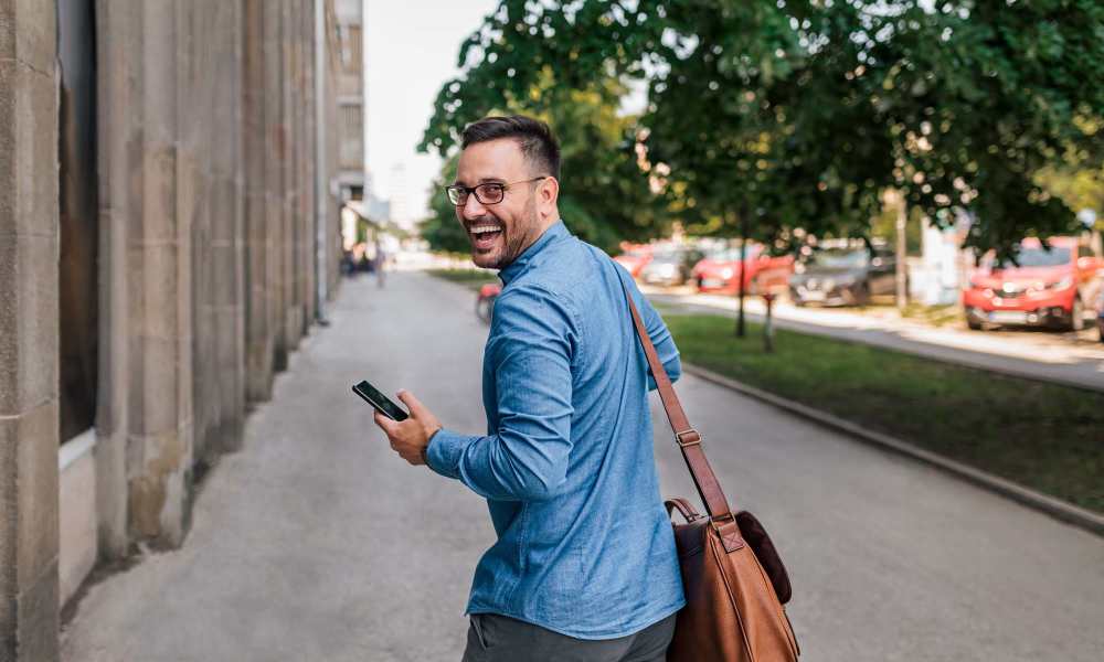 Man walking on sidewalk with phone and bag near Crescent Place in Savannah, Georgia