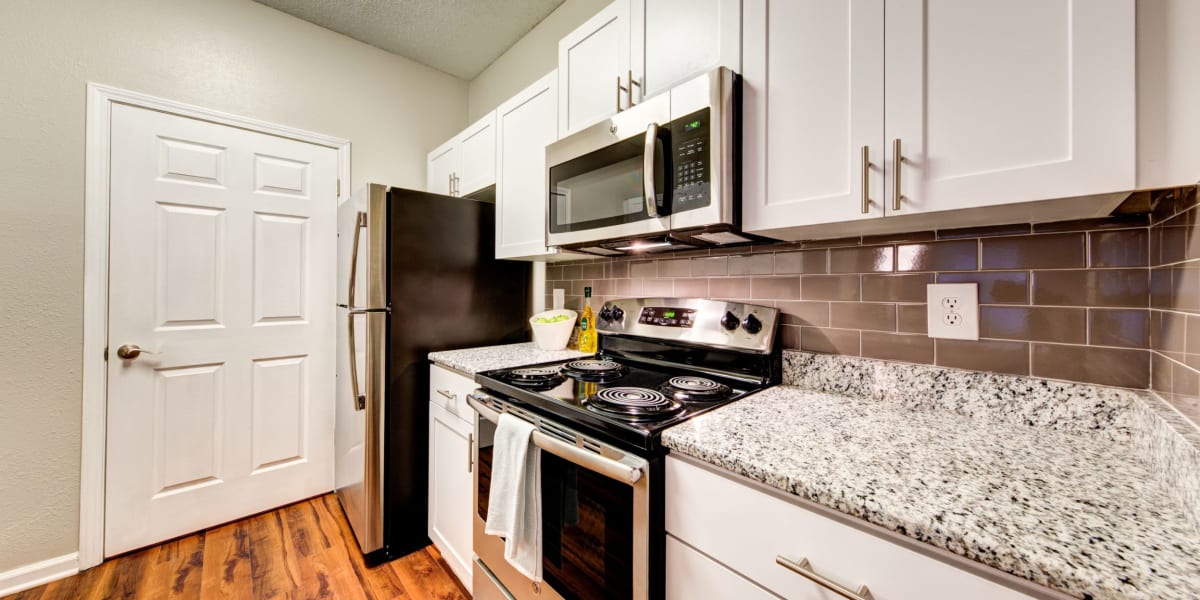 Open kitchen with granite counters, stainless steel appliances, and wood flooring at Marquis on Edwards Mill in Raleigh, North Carolina