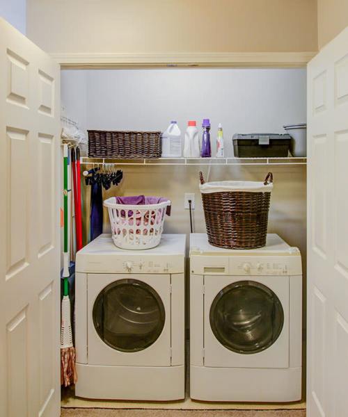 Laundry room with stacked washer and dryer, storage shelves, and organized cleaning supplies at Pennington Crossing in Johnson City, Tennessee