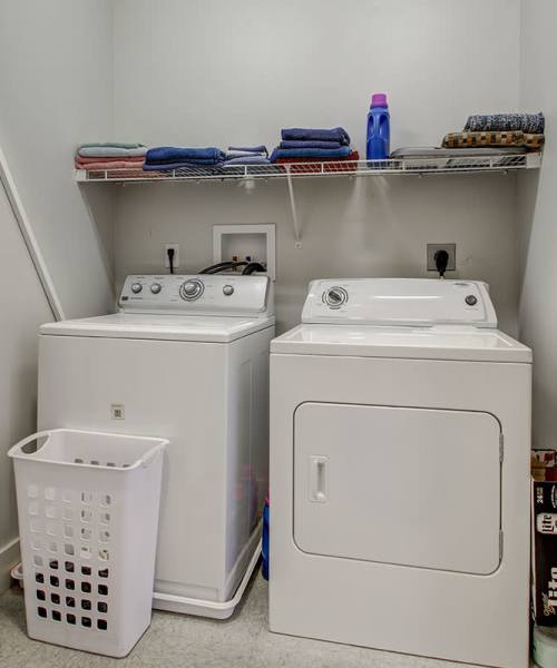 Laundry room with stacked washer and dryer, shelf with towels, and laundry basket at Lloyd House I in Menominee, Michigan