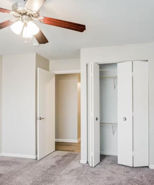 Spacious bedroom with ceiling fan, carpeted flooring, and closet with sliding doors at The Vinings at Christiana Apartments in Newark, Delaware