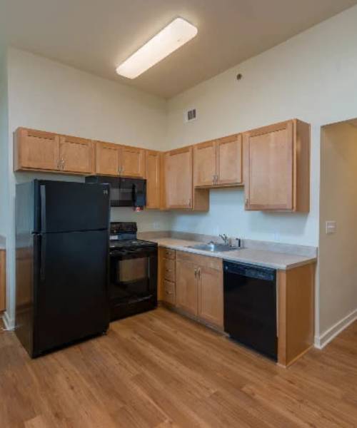 Kitchen with wood-style flooring and black appliances at A.L. Miller Village in Macon, Georgia